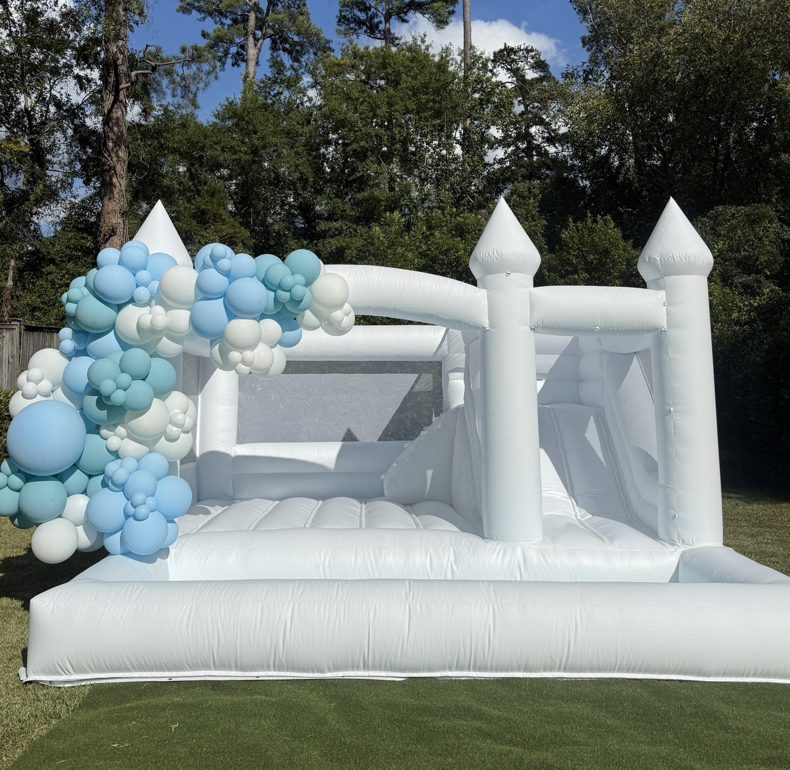 The Hartwell Grand, an all-white castle bounce house with a built-in slide and ball pit, styled with a blue and white balloon garland