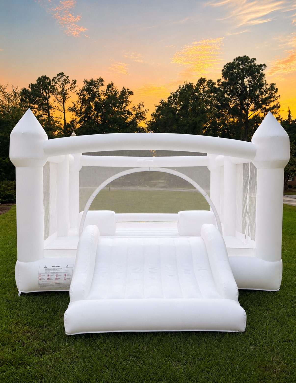 The Hartwell Mini, an all-white castle bounce house with a built-in slide, set up on a lawn at sunset